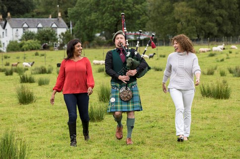 Two female tourists with bagpiper on grass, Scotland