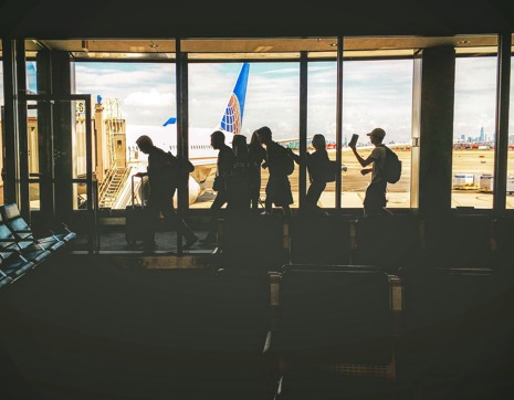 People silloutted in an airport terminal about to board a domestic flight. Read expert travel advice to see if you're REAL ID ready and set to go.