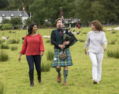 Scotland Bagpipe Tourists Walking With Piper On Green